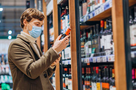 Young man in medical mask chooses wine for celebrationの写真素材