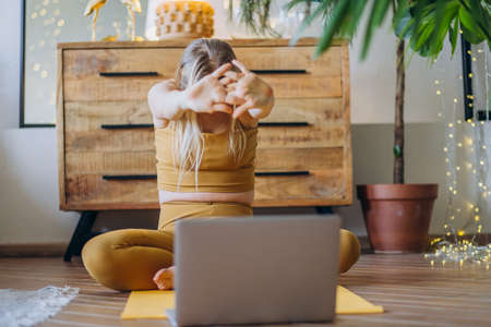 Blonde woman does yoga warm up on mat using online lassonの写真素材