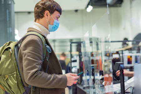 Man in medical mask stands near cash register with phoneの写真素材