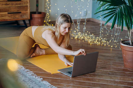 Young woman adjusts laptop to meditate on yoga mat at lessonの写真素材