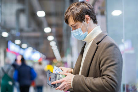 Young brunet man in medical mask counts money in walletの写真素材