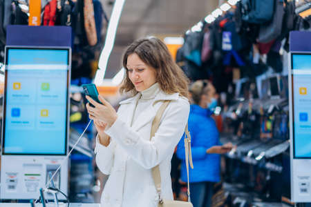 Woman with long curly hair chooses new phone in storeの写真素材