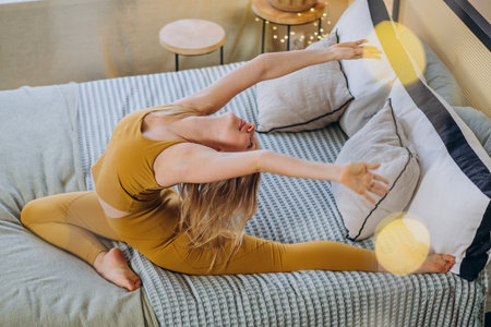 Young woman does yoga poses on blanket covering bedの写真素材