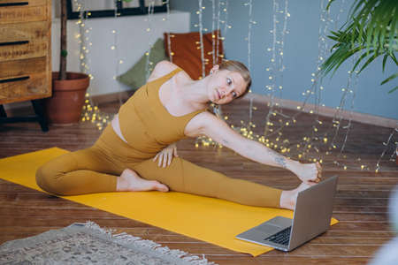 Young woman does yoga exercises on mat with online lasson