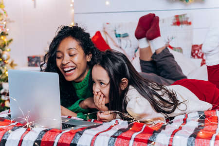 Brunette daughter and black mother chat using laptopの写真素材