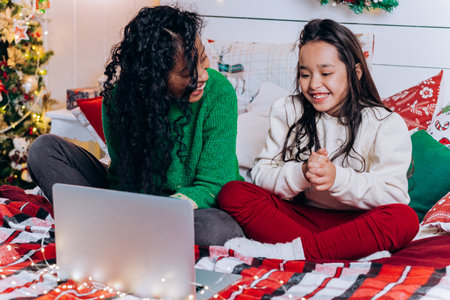 Daughter and black mother communicate using laptop on bedの写真素材