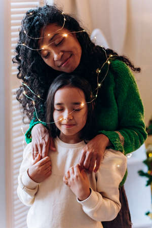 Girl and mother pose in garland against Christmas treeの写真素材
