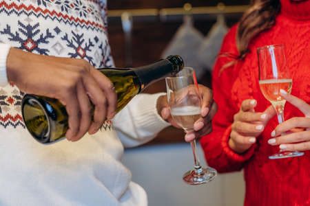 Black man and woman pour champagne in glasses for Christmasの写真素材