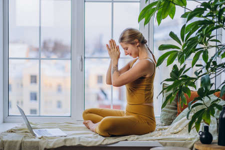 Young woman meditates sitting on windowsill at laptopの写真素材