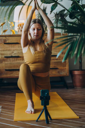Woman with blonde hair exercises on mat with phone on tripodの写真素材