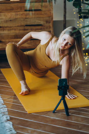 Woman with blonde hair exercises on mat with phone on tripodの写真素材
