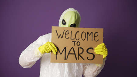 Green alien welcomes people to Mars holding cardboard signの写真素材