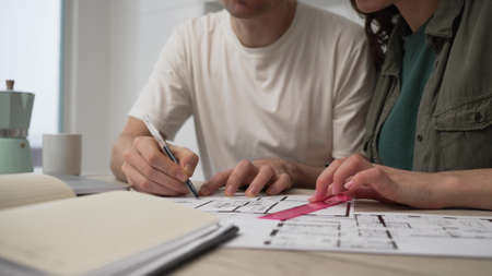 A married couple is actively discussing repairs in a new apartment or house while sitting at a table and making notes in a notebookの写真素材