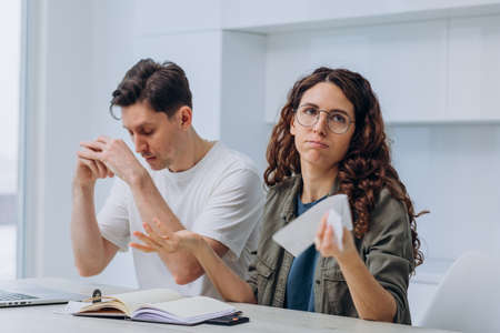 Husband and wife count the expense of finance at home in the kitchen at the table and write it down in a notebook, a woman with checks in her hands justifiesの写真素材