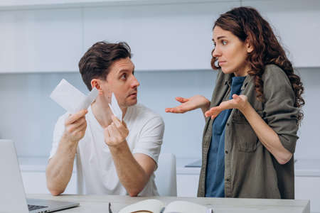 Husband shows his wife expensive checks and asks where the money went, the wife makes a helpless gestureの写真素材