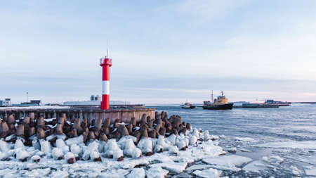 Lighthouse among breakwaters against sailing cargo shipsの写真素材