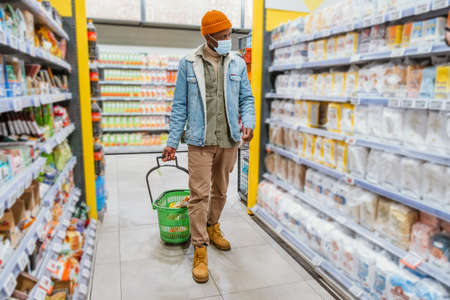 African-American man in mask walks past shelves in storeの写真素材