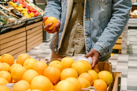 Young African-American customer takes orange fruits in storeの写真素材