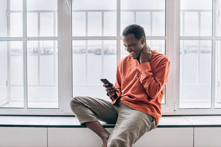 Black guy looks out of window holding phone in roomの写真素材