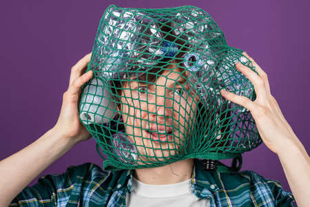 Portrait of a man with a mesh bag over his head with plastic bottles on a purple background