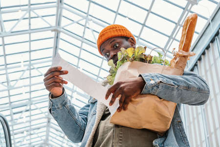 Surprised black man looks at receipt total with food in mallの写真素材