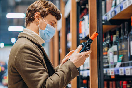 successful masked man reads the label on a bottle of wine in supermarketの写真素材