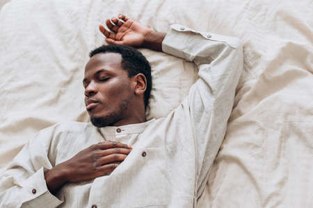 Calm African-American man in shirt sleeps on comfortable bedの写真素材