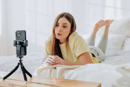 Female blogger with a bionic prosthetic arm leads an online broadcast or records an issue or communicates with friends by video call while lying on a bedの写真素材