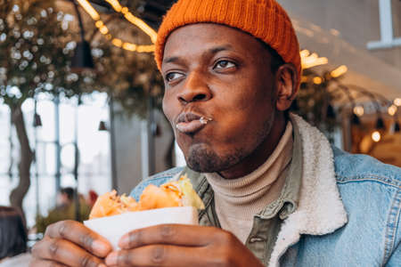Pleasured African-America guy eats tasty hamburger in cafe