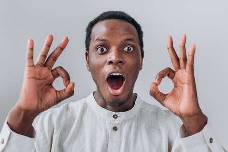 Emotional African-American guy shows thumbs up on light greyの写真素材