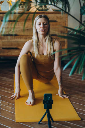 Woman with blonde hair exercises on mat with phone on tripodの写真素材