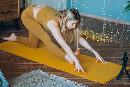 Woman with blonde hair exercises on mat with phone on tripodの写真素材