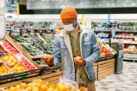 African-American man in mask takes lemon in supermarketの写真素材