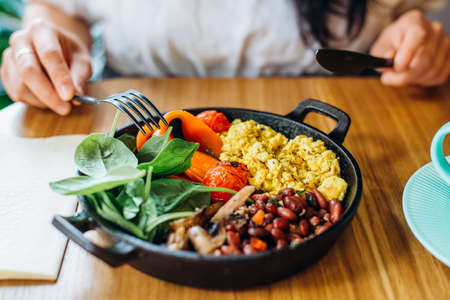 Vegan food in frying pan and woman hands with fork and knifeの写真素材