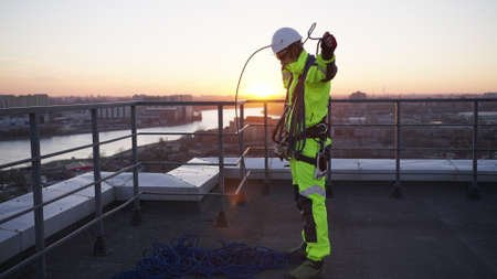 Industrial climber on rooftop hangs safety rope on shouldersの写真素材