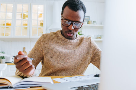 Young African American man works online at a laptop and writes down information in a notebookの写真素材