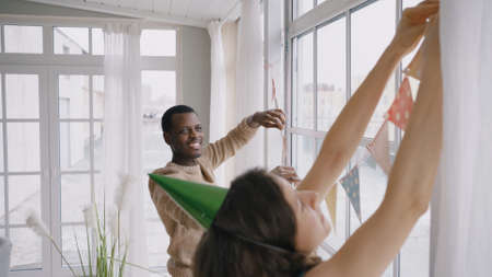 Multinational couple hangs colorful pennant banners in roomの写真素材