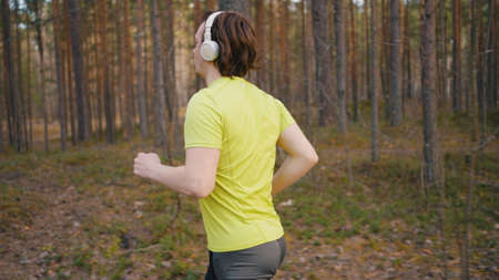 Young man in wireless headphones runs through pine forestの写真素材