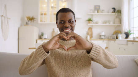 Happy man shows love making heart shape gesture on sofaの写真素材