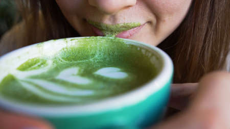 Woman drinks matcha latte in cafe and foam stays on lipsの写真素材