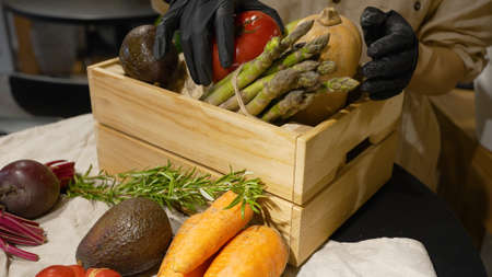 Woman in rubber gloves fills wooden box with vegetablesの写真素材