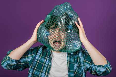 Man with a mesh bag on his head and plastic bottles is holding his head with a frightened expression...