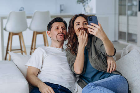 Cheerful couple taking a selfie on the phone while sitting on the couch togetherの写真素材