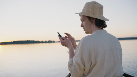 Man tries to get cell signal on smartphone against lakeの写真素材