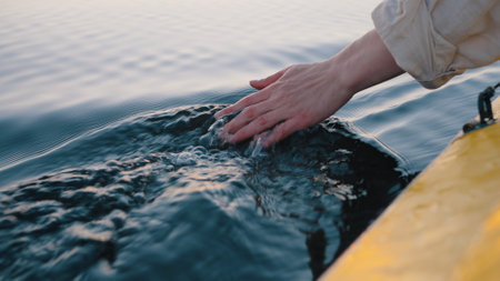 Person dips hand in calm river water sitting in sailing boatの写真素材