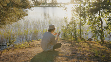 Young man surfs internet on smartphone sitting on river bankの写真素材
