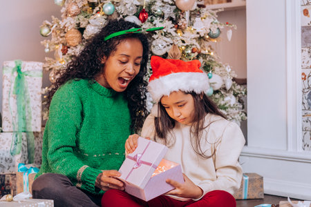 Daughter and mother in Christmas hats open presentsの写真素材