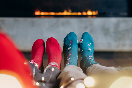 christmas cosiness against the background of an electric fireplace, a couple in red and green socks with garland, minimalismの写真素材