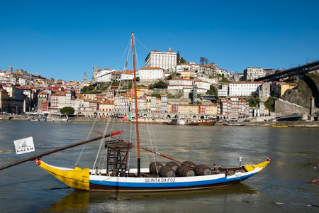 A colorful Rabelo boat, traditionally used to transport wine barrels, floats on the Douro River against the backdrop of Portos historic cityscape.のeditorial素材