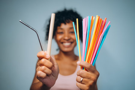 A cheerful woman compares a reusable metal straw with colorful plastic straws, highlighting the...